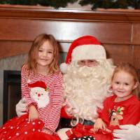 Two daughters of alumni sitting with Santa.